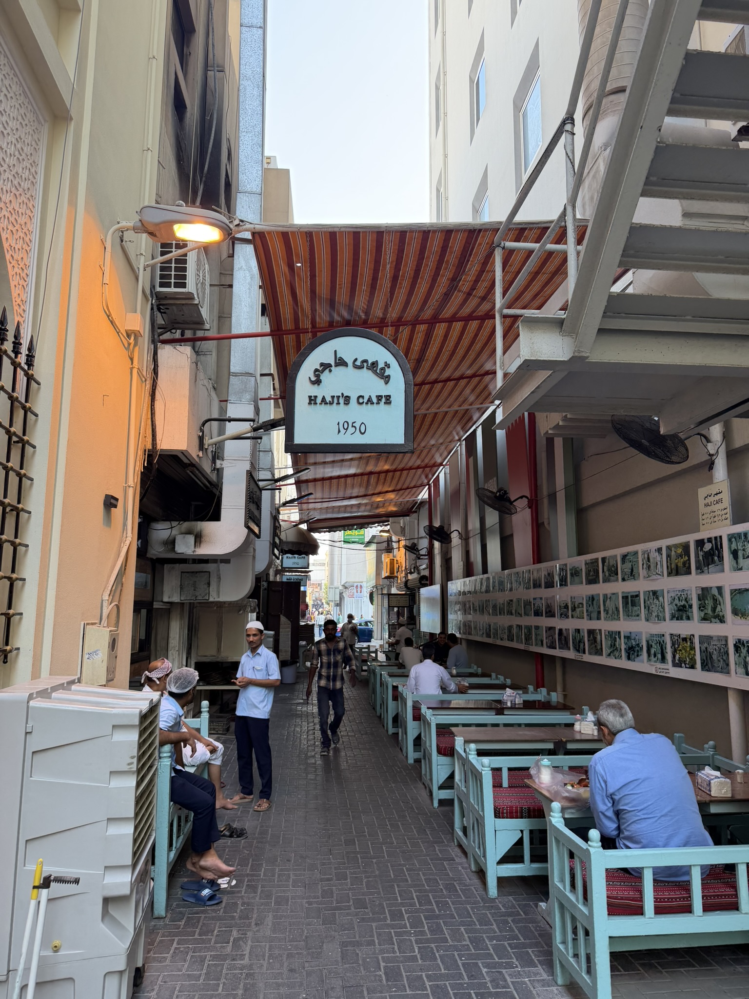 The Haji's Cafe sign hanging over a narrow souk alley lined with turquoise benches