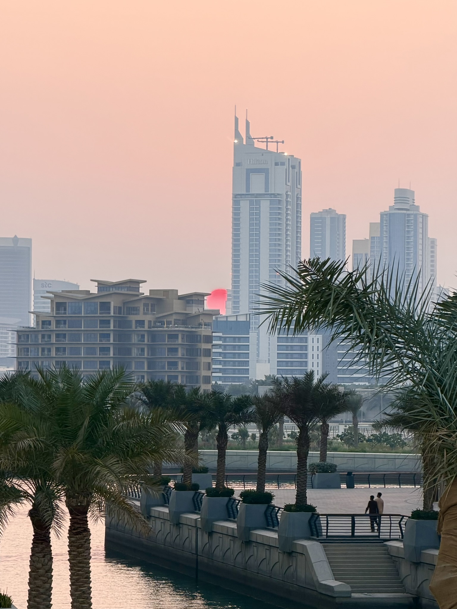 A pink and orange sunset over the Manama waterfront, palms and skyline in silhouette