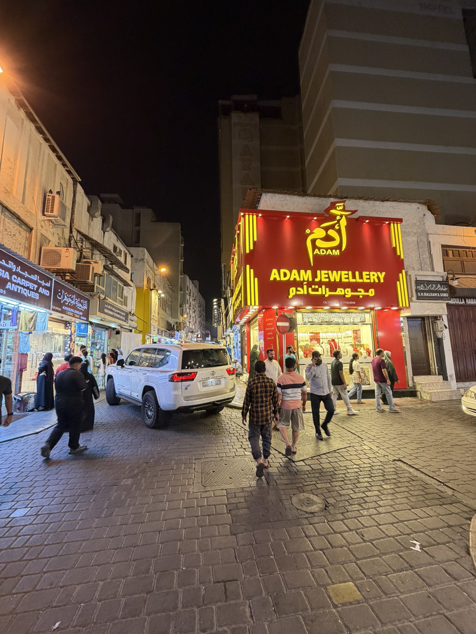 A lit night street in the souk with a jewelry store glowing and people walking