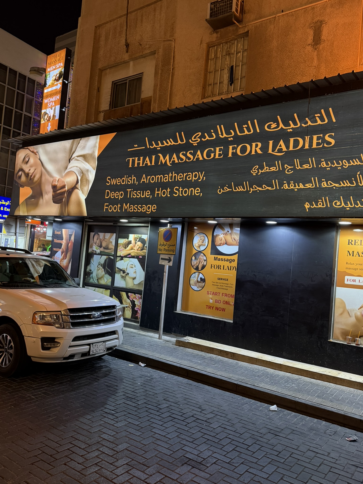 A brightly lit spa storefront advertising massage for ladies at night