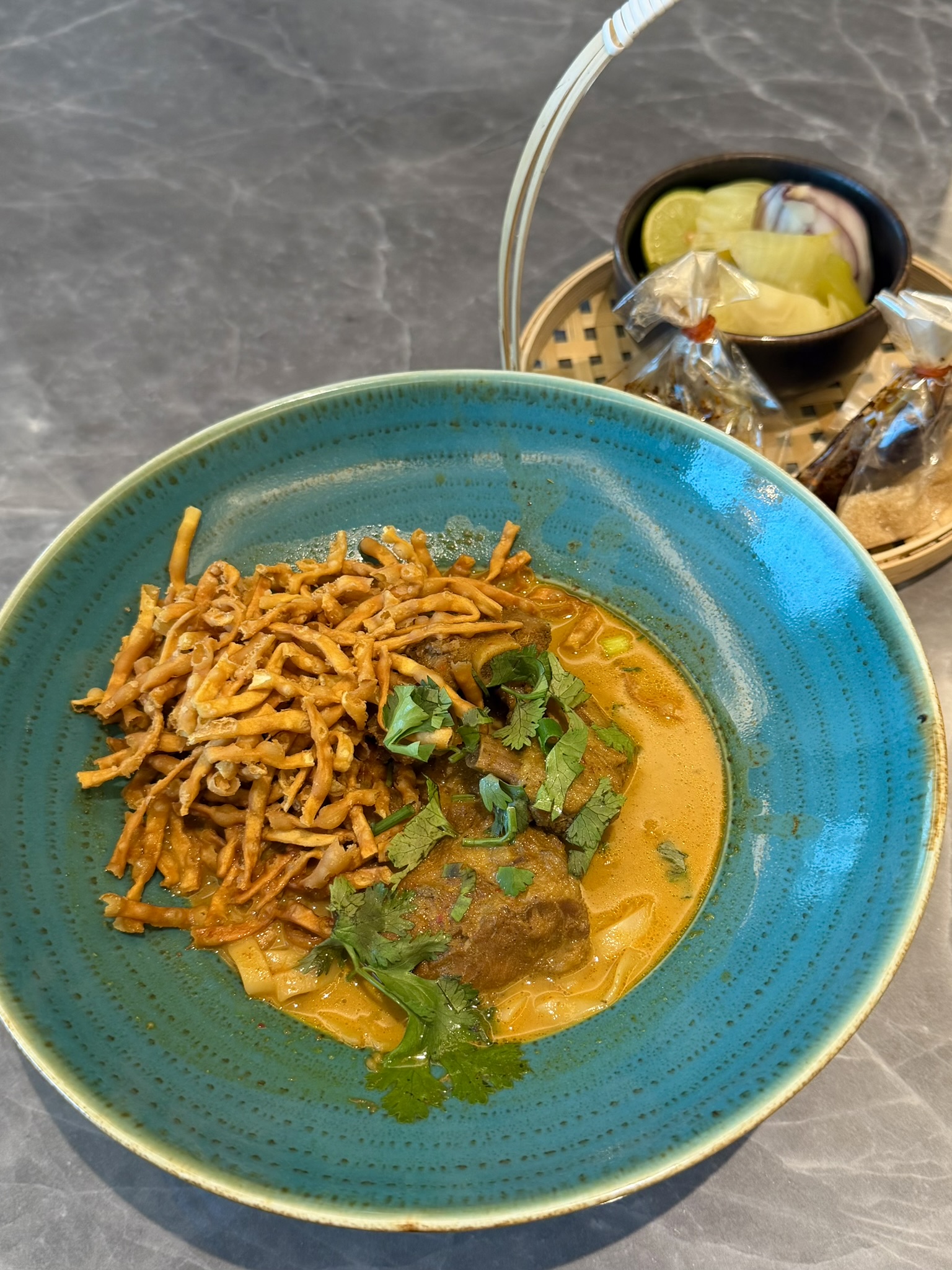 An elevated Khao Soi presentation in a turquoise bowl