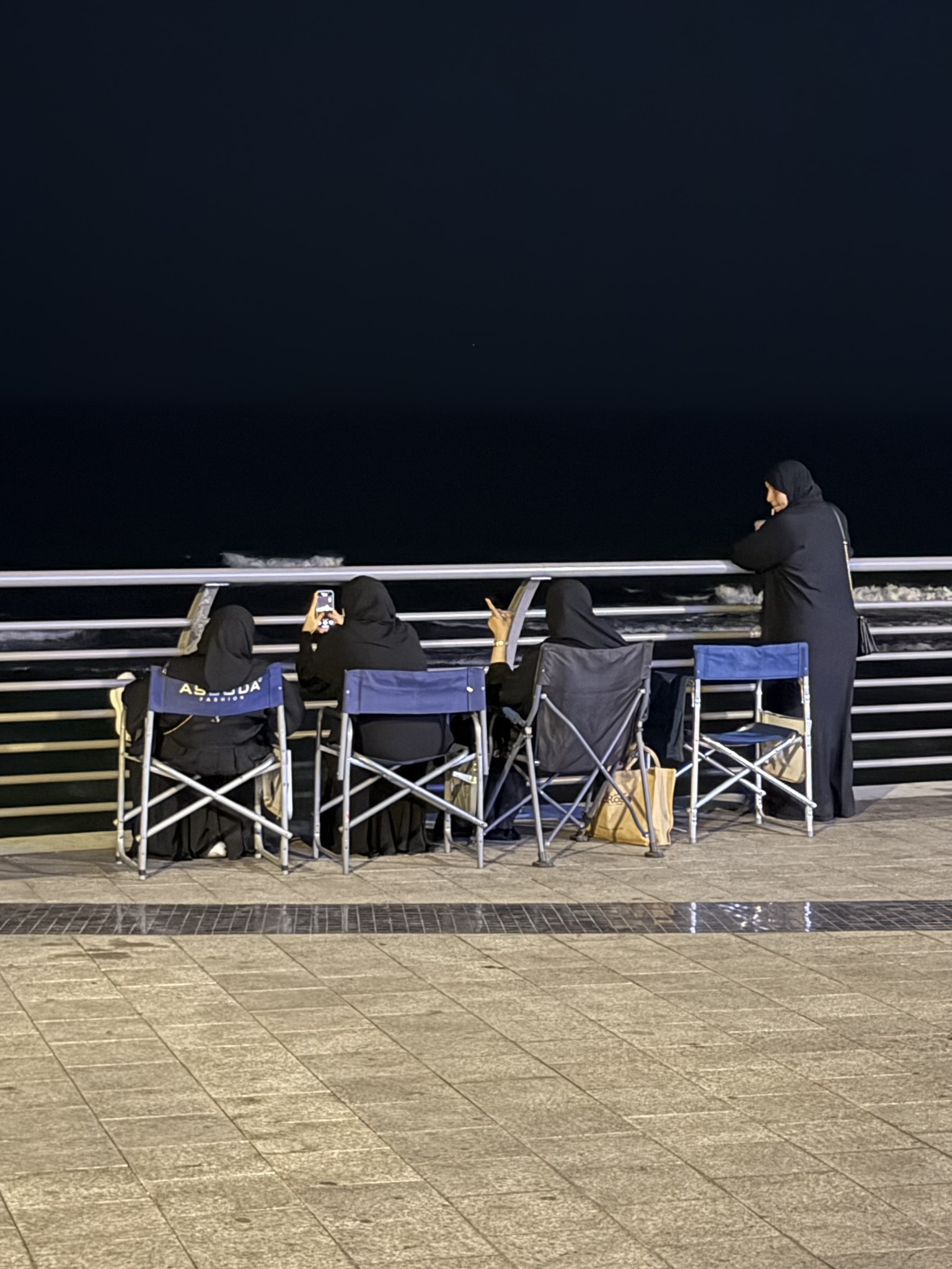 Women in abayas sitting by the sea at the Corniche