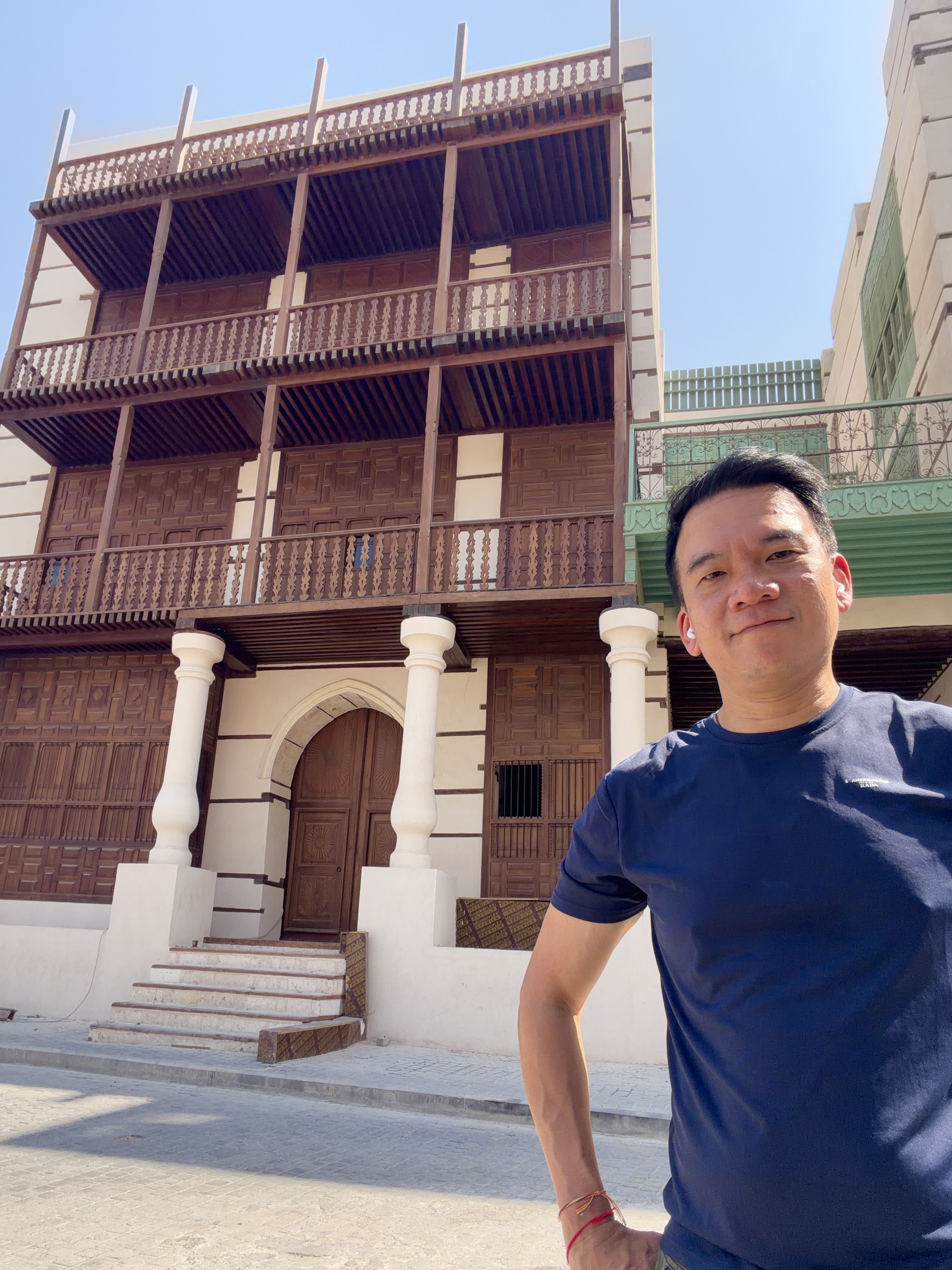 In front of a traditional brown wooden building in Al Balad