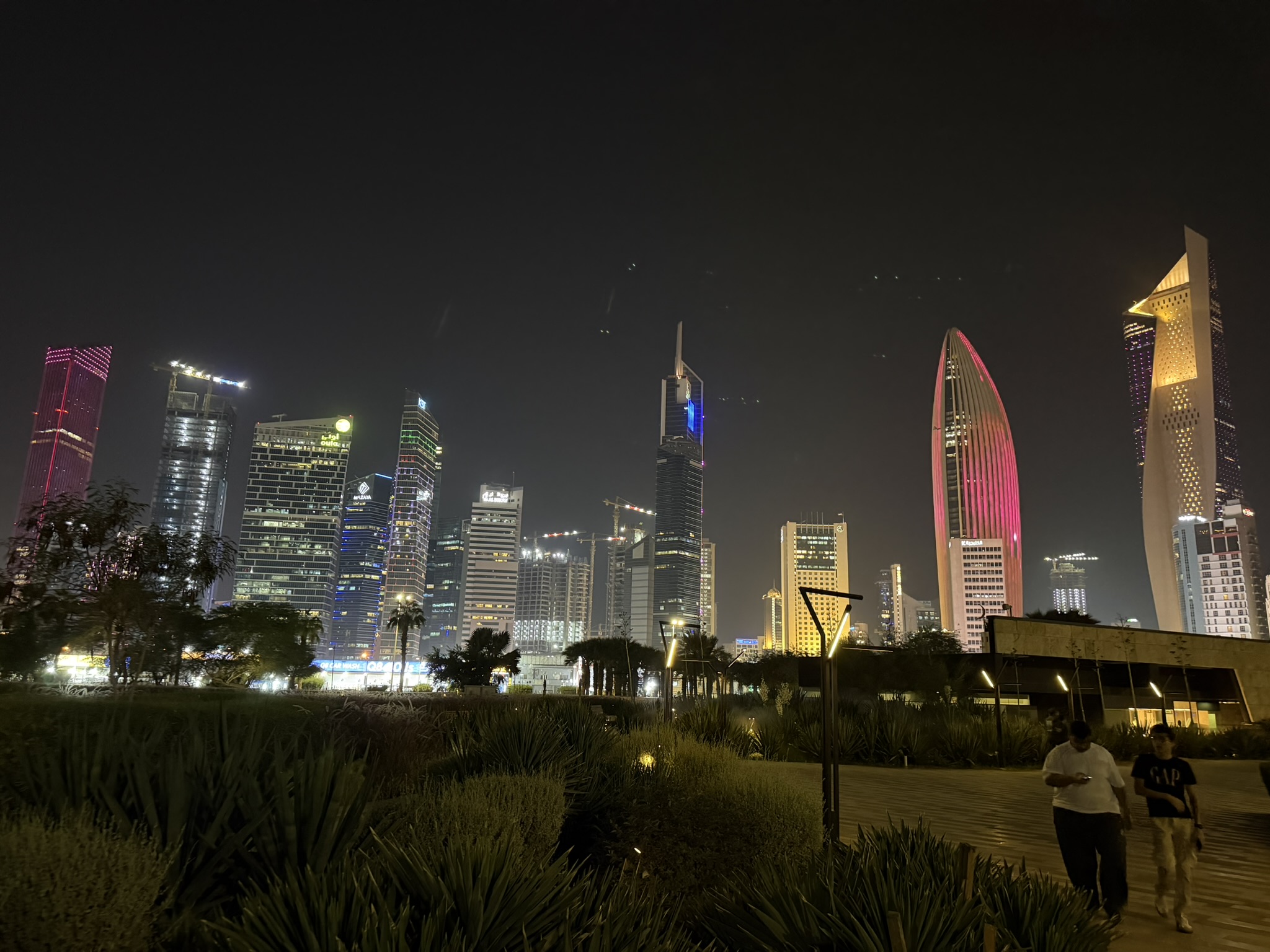 Kuwait City skyline lit up at night, seen from a park path