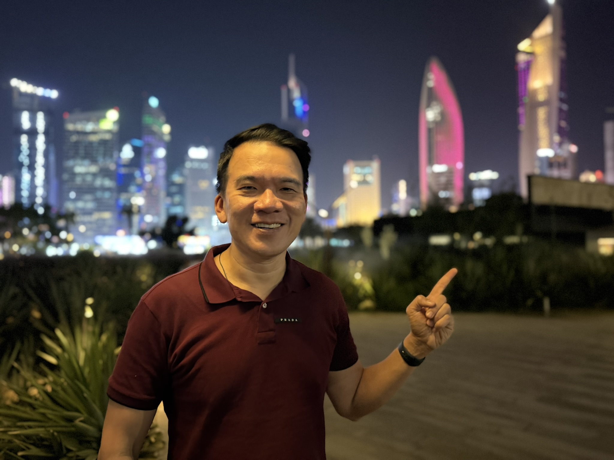 Pointing toward the neon-lit Kuwait City waterfront skyline at night