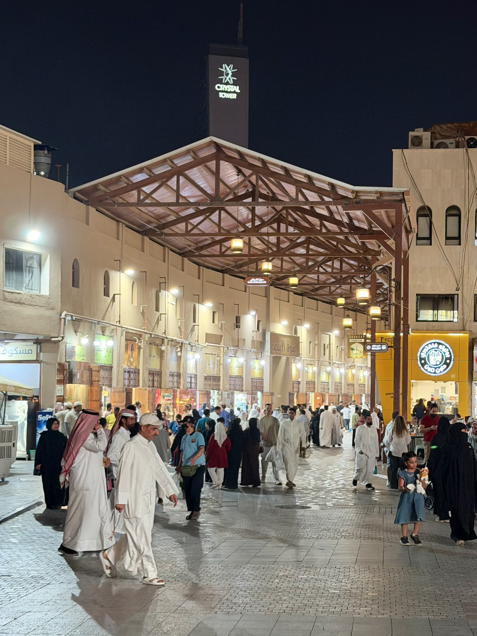 Crowded Souq Al-Mubarakiya market street at night beneath Crystal Tower