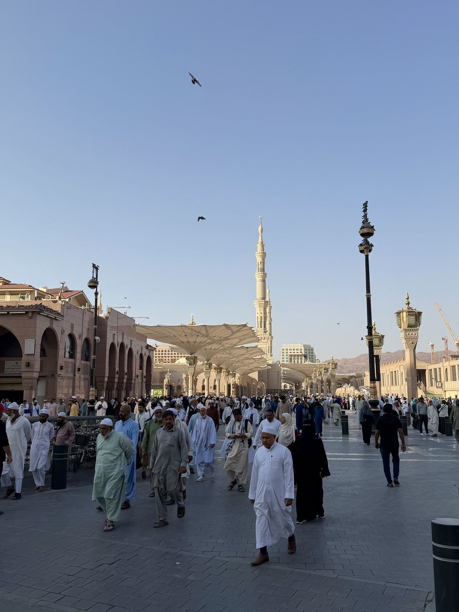 Crowds walking near Al-Masjid an-Nabawi with the iconic umbrella structures
