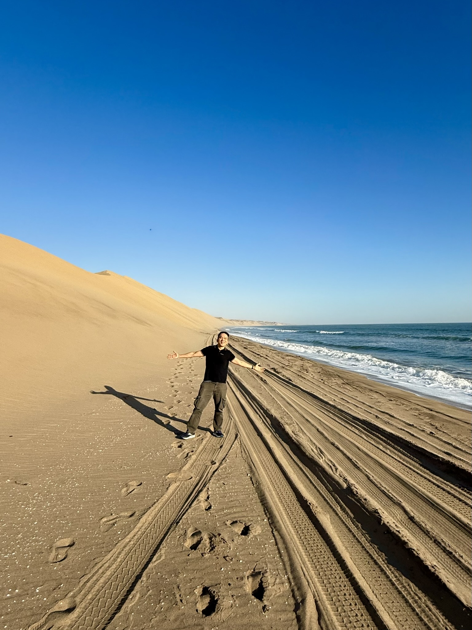 Arms spread wide on the beach between dunes and ocean