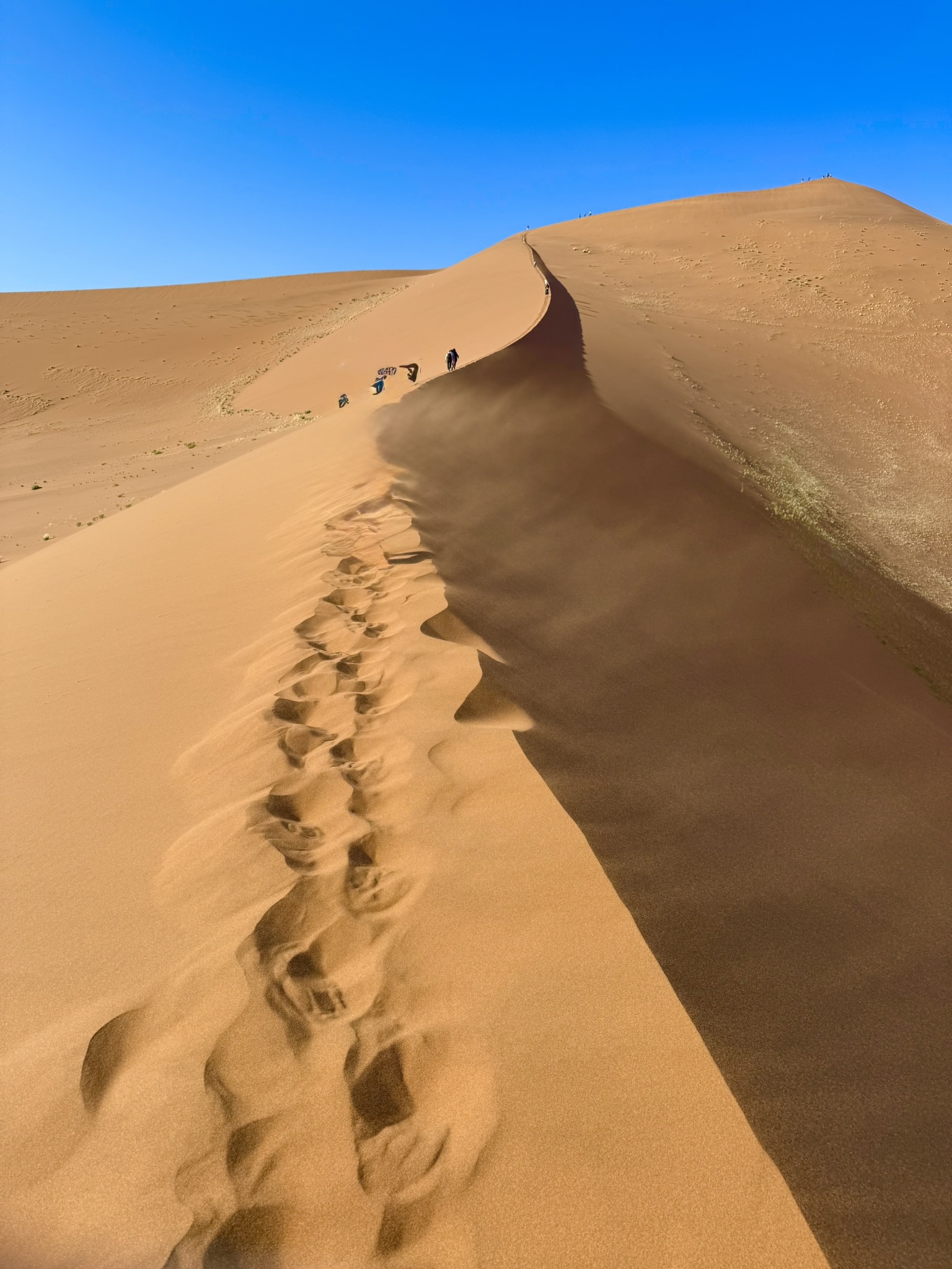 Dramatic dune with footprints leading up, wind blowing sand
